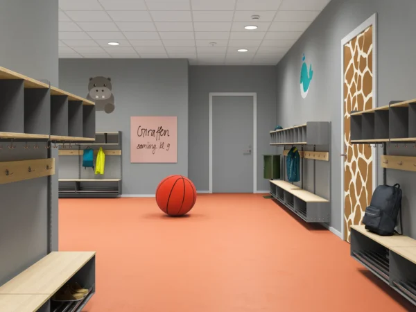 Förskolekorridor med orange golv och grå väggar, dekorerad med en blå val och en flodhäst på väggen. Inredningen består av svarta hyllor med träpaneler, krokar och bänkar. En dörr med giraffmönster finns till höger. På väggen sitter en rosa skylt med texten 'Giraffen samling kl 9'. En stor leksaksbasketboll ligger i mitten av rummet.