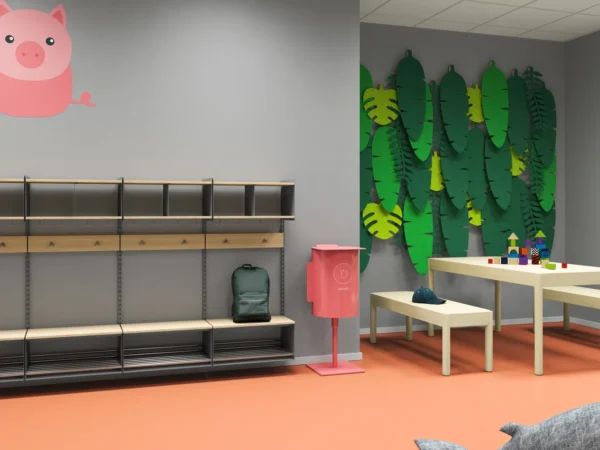 Förskolehall med orange golv, grå väggar och en blå val som väggdekoration. Till vänster syns klädhängare med jackor och ett rosa konstverk. Längs väggen finns sittbänkar med förvaringsfack och krokar ovanför. En grön soptunna märkt 'organic' står vid väggen, och en stor leksaksbasketboll ligger på golvet.